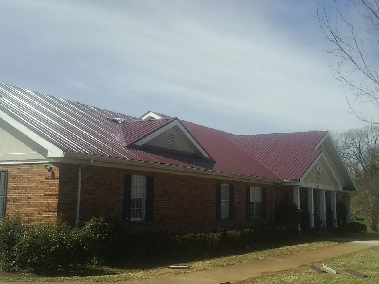 Red metal roof with gabled entries on a long brick building, from a Hail Damage Roof Repair job in Dillon