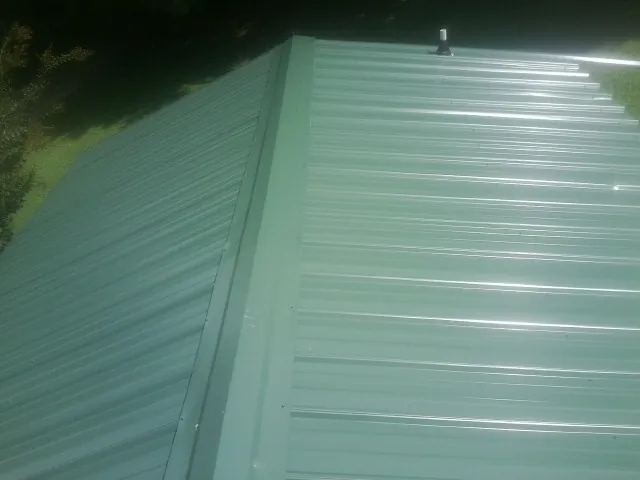 New green metal panels meeting at the ridge of a roof — Flat Roof Repair work by our crew in Dillon